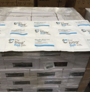 A stack of cardboard boxes on a pallet, wrapped in clear plastic, with several white hybag flat absorbent pads and desiccant bags laid out on top.