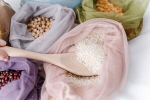 A wooden spoon scooping white rice from a mesh bag, surrounded by other mesh bags filled with dried beans, grains, and legumes—showcasing efforts to protect rice exports amid a colorful variety of pantry staples.