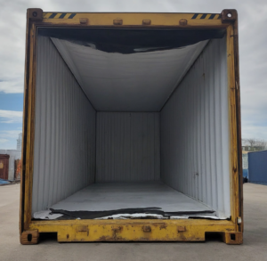 A large, empty yellow temperature-controlled shipping container with an open front reveals a white interior lining and some torn material at the entrance, sitting outdoors on a concrete surface.