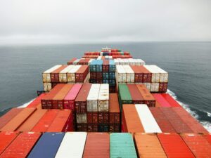 Aerial view of a large cargo ship at sea, loaded with colorful shipping containers, showcasing solution driven expert packaging as it heads toward the horizon under a cloudy sky.