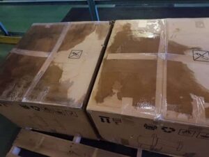 Two large cardboard boxes on a wooden pallet, both showing significant water damage with dark, wet patches—highlighting the need for the best desiccant for shipping container protection against moisture.